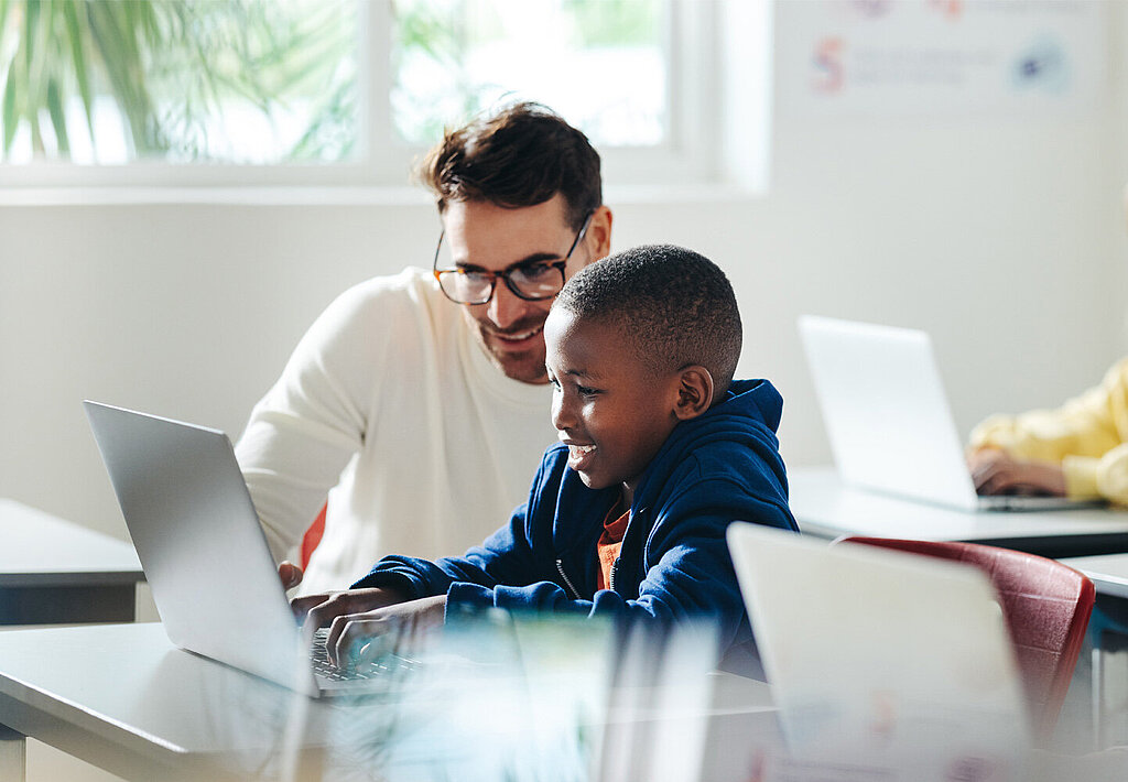 Ein Lehrer und ein Schüler arbeiten an einem Laptop in einem Klassenzimmer.