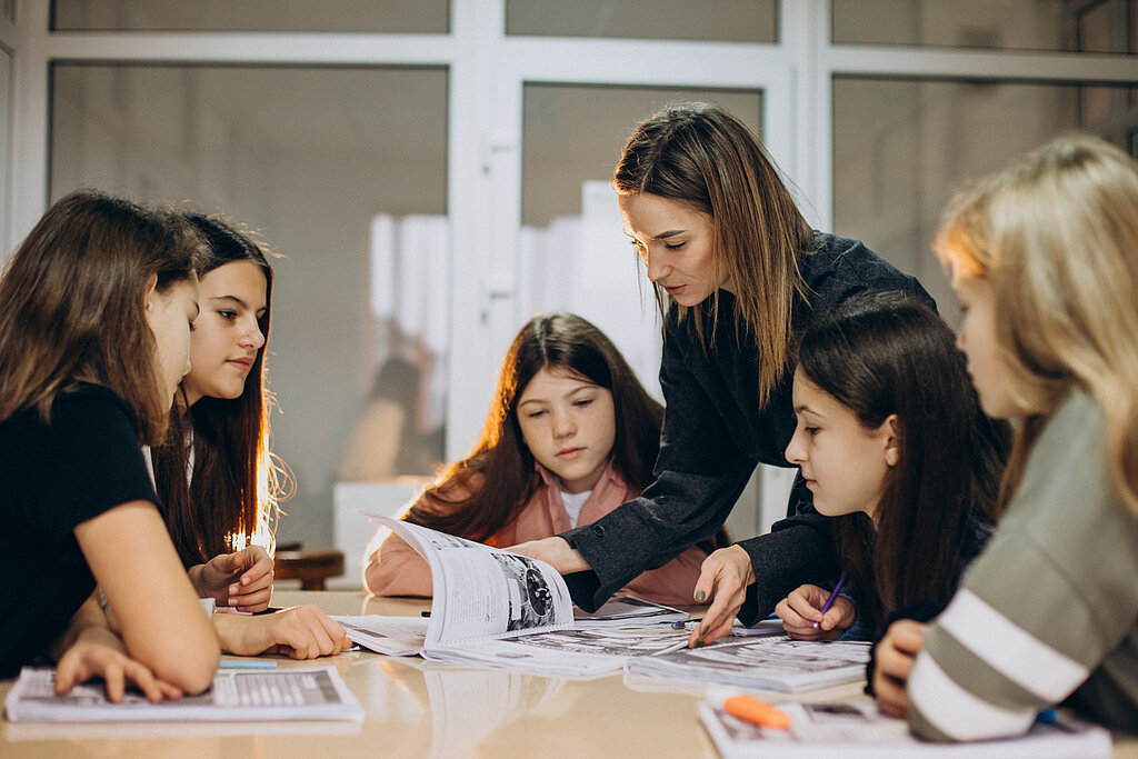 Lehrerin und Schülerinnen sprechen miteinander.