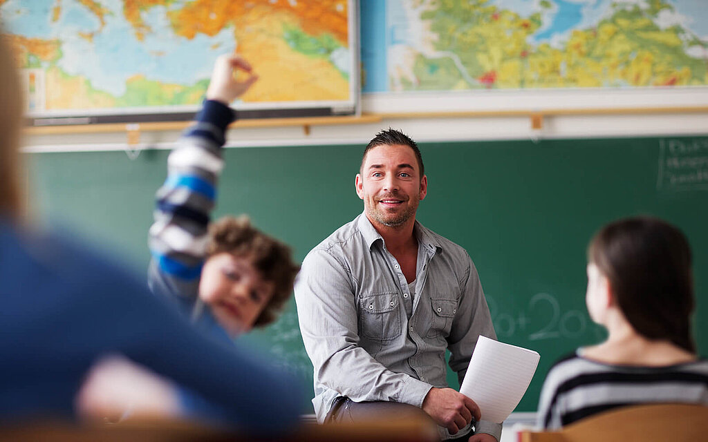 Lehrkraft zeigt Präsenz im Schulunterricht und ein Schüler hebt die Hand. 